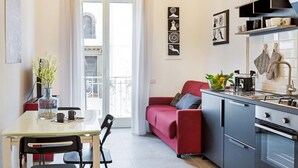 Une cuisine compacte dotée d’appareils électroménagers modernes, un coin repas avec une table en verre et un canapé rouge.