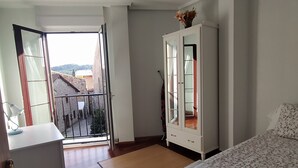 Un dormitorio con cama, armario, escritorio y balcón.
