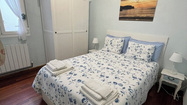 Un dormitorio con cama, mesita de noche, armario, ventana con cortinas e imagen colgada en la pared.