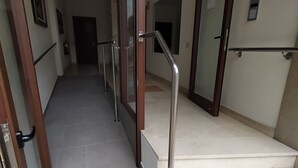 Una entrada de edificio moderna con puerta de vidrio, barandilla metálica y piso de baldosas.