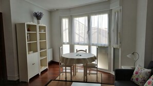 Una habitación con una mesa de comedor, sillas, un sofá, una estantería y una ventana con cortinas.