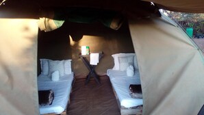 A tent with two beds, a table with a towel, and a small shelf with items. - Pop Lamont Camp (Ngoma)