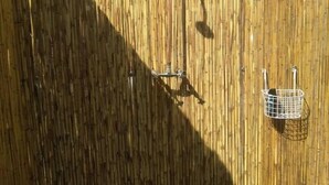 A bamboo fence with a metal bird feeder and a hanging light fixture. - Pop Lamont Camp (Ngoma)
