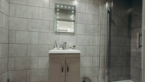 Une salle de bain moderne équipée d’une douche, d’un meuble-lavabo avec miroir et de toilettes.