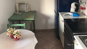 A compact kitchen with a green table, a white tablecloth, and a bouquet of flowers. - THE TERRACE ON THE CREW (Santa Teresa Gallura)
