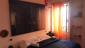 A bedroom with a large bed, a nightstand, a lamp, a wall-mounted TV, and a window with curtains. - THE TERRACE ON THE CREW (Santa Teresa Gallura)