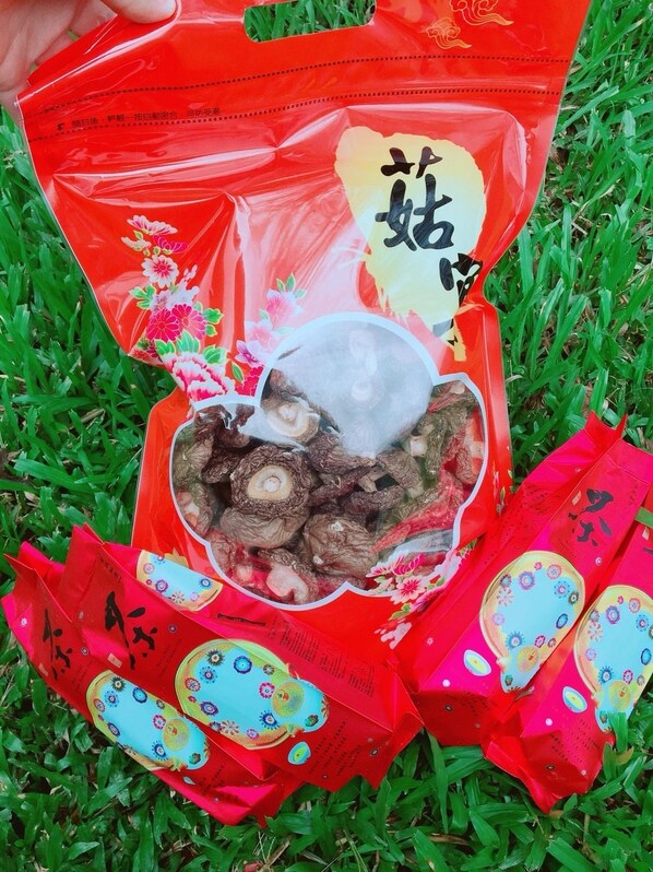 A red package with a transparent window, containing dried mushrooms, placed on grass.