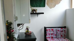 A small, compact room with a tiled floor, a black sofa with patterned cushions, a small table with a decorative item, and a wall-mounted shelf with flowers. - Exclusive apartment with terrace (Padova)