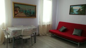 A living room with a red sofa, a dining table with chairs, and two paintings on the walls. - Exclusive apartment with terrace (Padova)