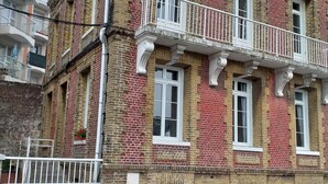 Un edificio de varios pisos con fachada de ladrillo, marcos de ventana blancos y un balcón con barandilla blanca.