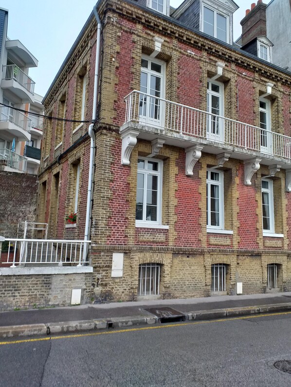 A multi-story building with a brick facade, white window frames, and a balcony with a white railing.