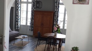 Una sala de estar con sofá, una mesa de centro y una zona de comedor con sillas y una mesa. Se observa un aparador de madera y una planta en maceta.