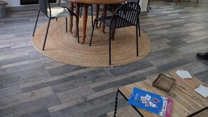 Un comedor con una mesa redonda de madera rodeada de sillas, un tapete tejido y un jarrón de flores.