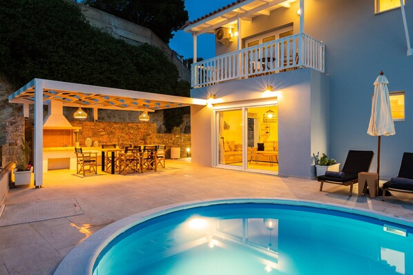 A poolside area with a covered patio, outdoor seating, and a two-story building with a balcony.