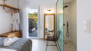 Et moderne hotelværelse med seng, trækommode, bøjlestang og brusekabine i glas, samt udsigt til det fri.