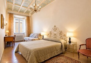 A hotel room with a bed, two bedside lamps, a desk with a chair, a window with curtains, and a chandelier. - Domus Antiqua 100 sqm - charming apartment at the Pantheon. Free Wi Fi Internet (Roma)