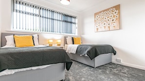 A bedroom with two beds, a large window with blinds, a wall-mounted artwork, and a carpeted floor.