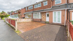 A residential street with terraced houses, a paved driveway, and a parked car.