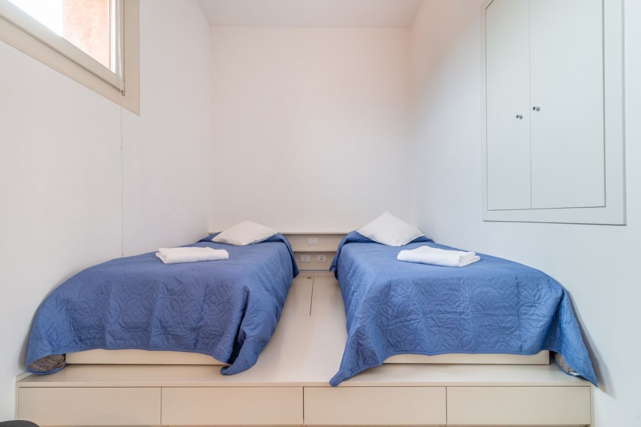 Une petite chambre avec deux lits simples, chacun recouvert d’une couverture bleue et agrémenté d’oreillers blancs.