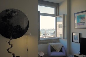 Enjoy a serene view of the water from this room's large window, featuring a wall-mounted mirror and a flat-screen TV.