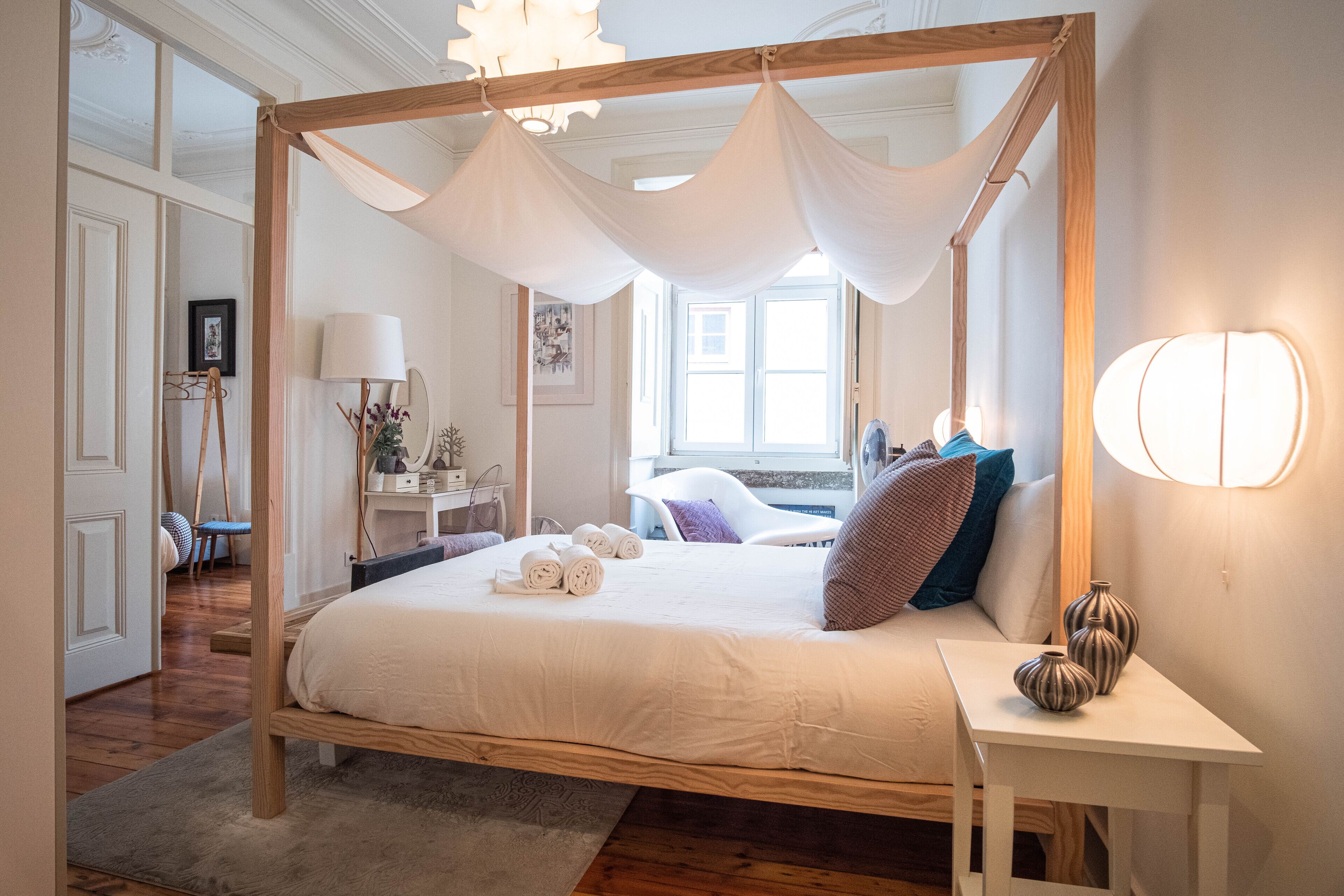 Uma cama com dossel e cortina, uma mesa de cabeceira com vasos, e vista para o interior do quarto.