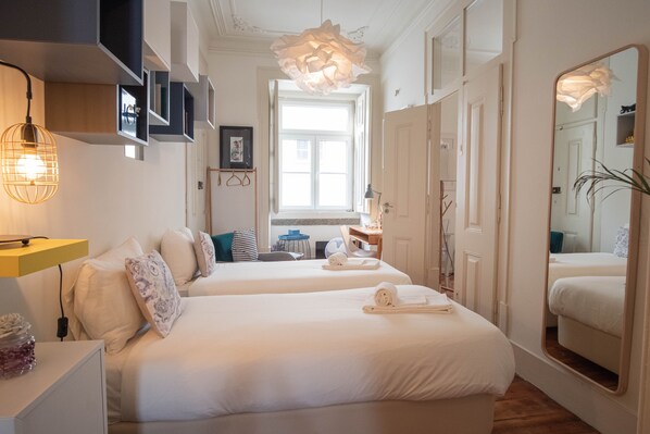Two beds with white linens and decorative pillows, a large mirror, and a chandelier adorn this stylish room.