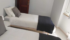 A small, compact room with two single beds, each with pillows and a blanket. - Renovated apartment right in the city center (Lagos)