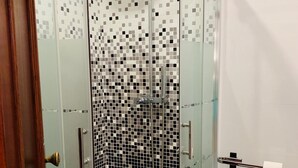 A glass-enclosed shower with a tiled mosaic wall, a white sink, and a toilet paper holder. - Renovated apartment right in the city center (Lagos)