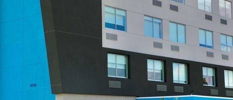A modern hotel building with a blue and grey facade, a prominent 'tu' logo, and a 'byHiton' sign.