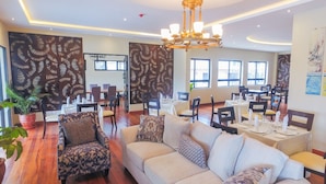 Eine geräumige Hotelhalle mit einer großen Couch, Sesseln und Esstischen für die Gäste.