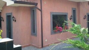 A house with a pink facade, a tiled roof, and a window with flowers. - B&B immersed in the Green (Nicolosi)