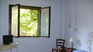 A room with a bed, a desk with a computer, a chair, a lamp, and a window with a view of trees. - B&B immersed in the Green (Nicolosi)