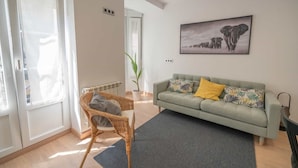 A living room with a green sofa, a wicker chair, a grey rug, and a painting of elephants on the wall. - La Fontina de Luarca (Luarca)