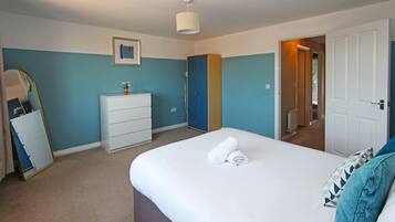 A bedroom with a bed, a dresser, a mirror, and a door leading to another room.