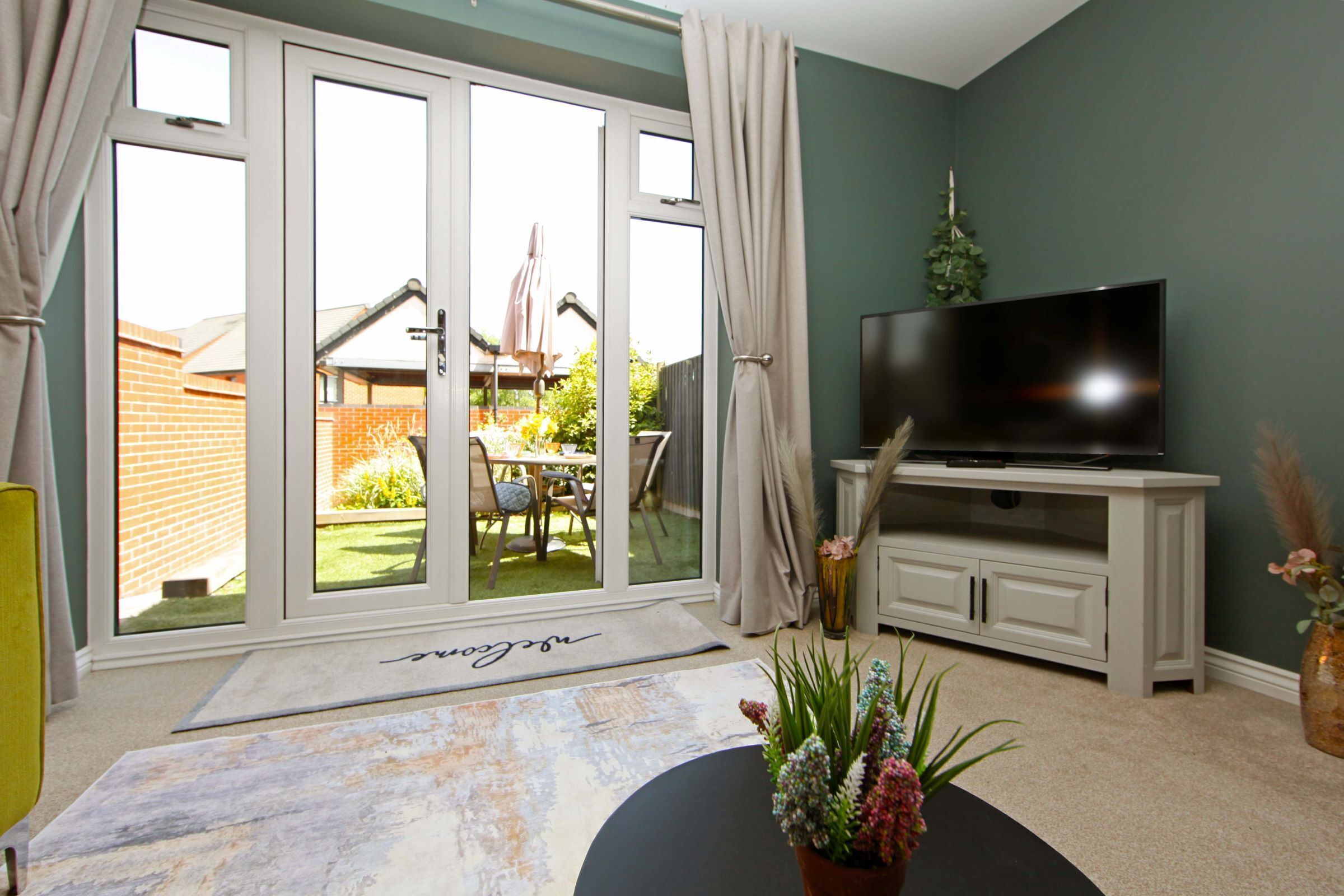 A living room with a television on a white cabinet, a sliding glass door leading to a patio, and a rug with a name on it.