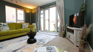 A living room with a green sofa, a coffee table, a flat-screen TV, and a large window with curtains. - Autumn Heights Apartments (Telford)