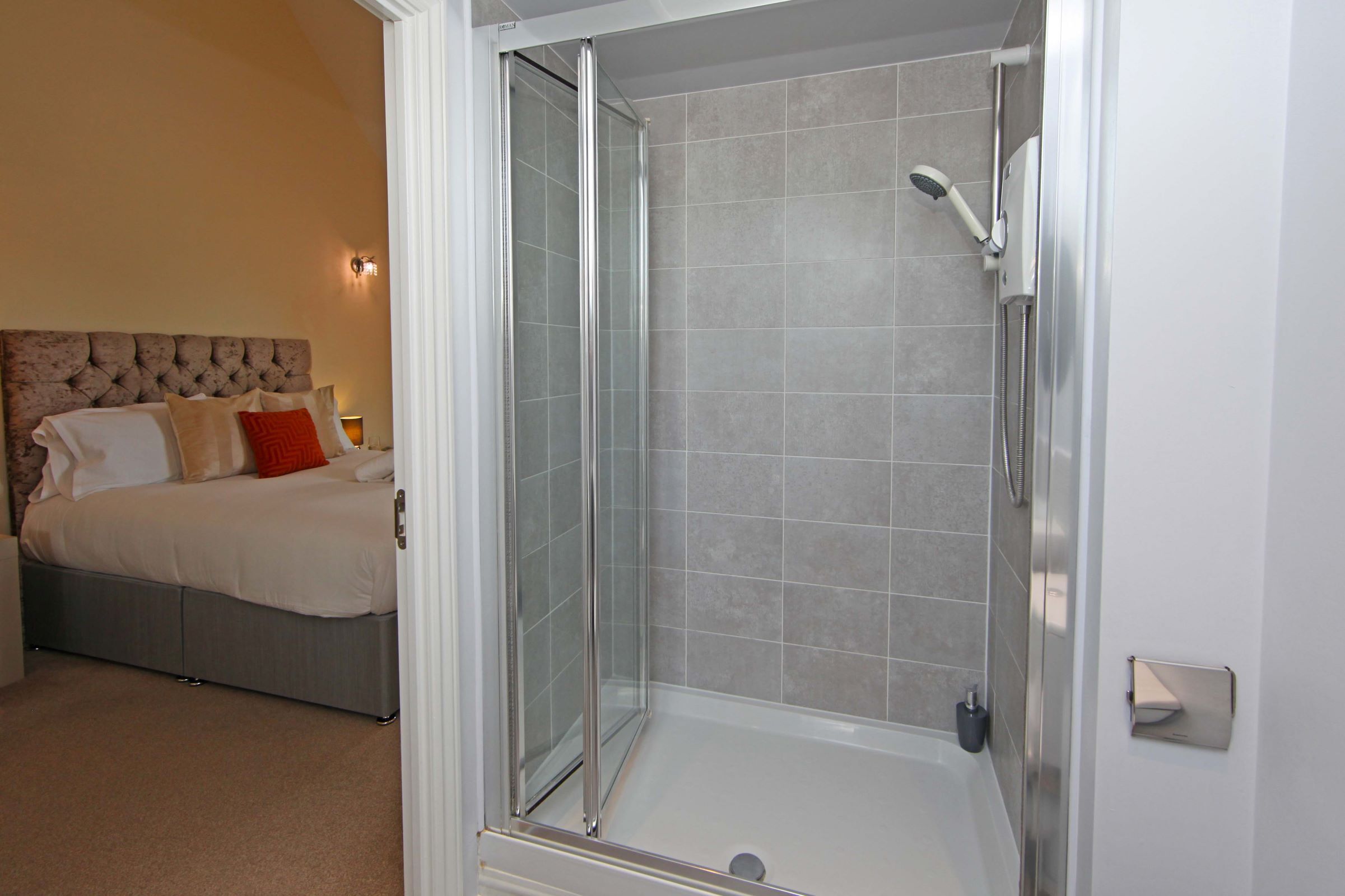 A bedroom with a bed, a glass-enclosed shower, and a nightstand.