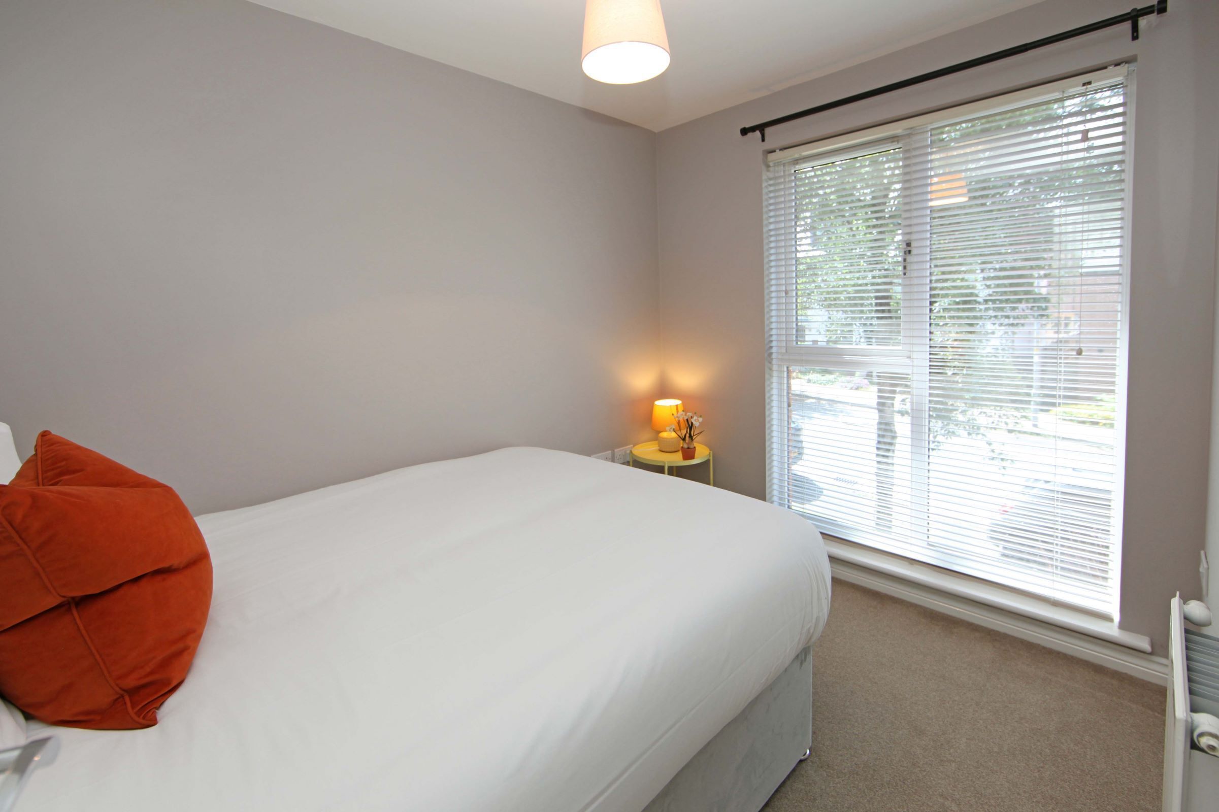 A bedroom with a bed, a nightstand, a lamp, and a window with blinds.