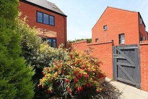 A residential area with two brick houses, one with a visible window and a door, and a well-maintained garden with various plants and flowers. - Autumn Heights Apartments (Telford)