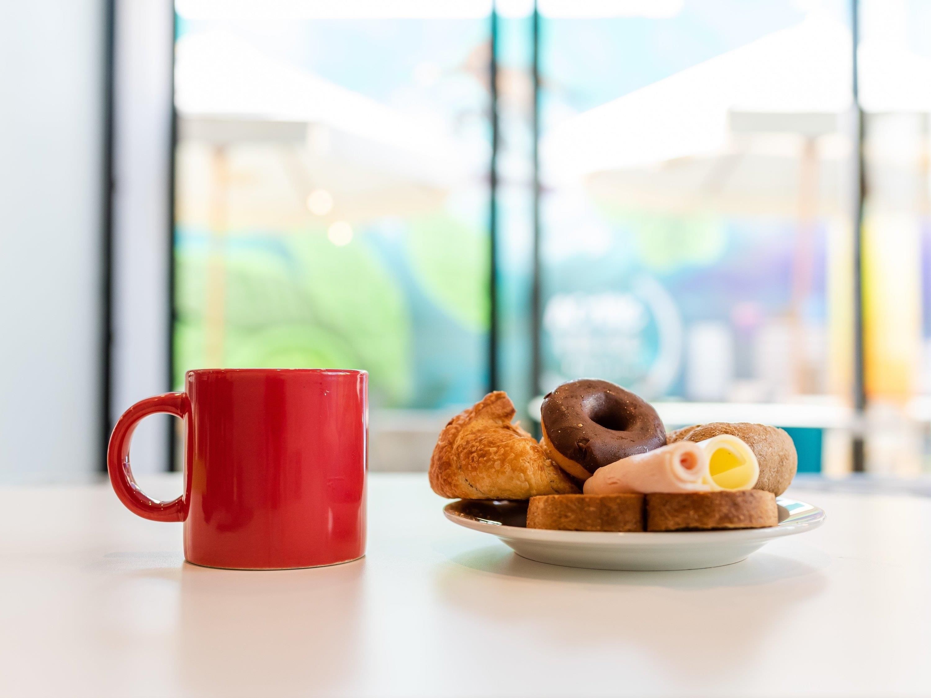 A red mug and a plate with assorted pastries on a table.