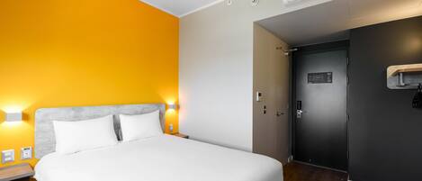 Habitación de hotel con cama, mesita de noche, lámpara de pared, equipo de aire acondicionado y puerta.