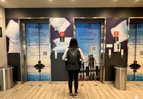 Una persona de pie frente a un ascensor con carteles promocionales que anuncian descuentos y servicios del hotel.