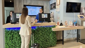 Vastaanottotiski, jossa on digitaalinen näyttö, litteänäyttöinen televisio ja kyltti, jossa lukee ”Recepción”.