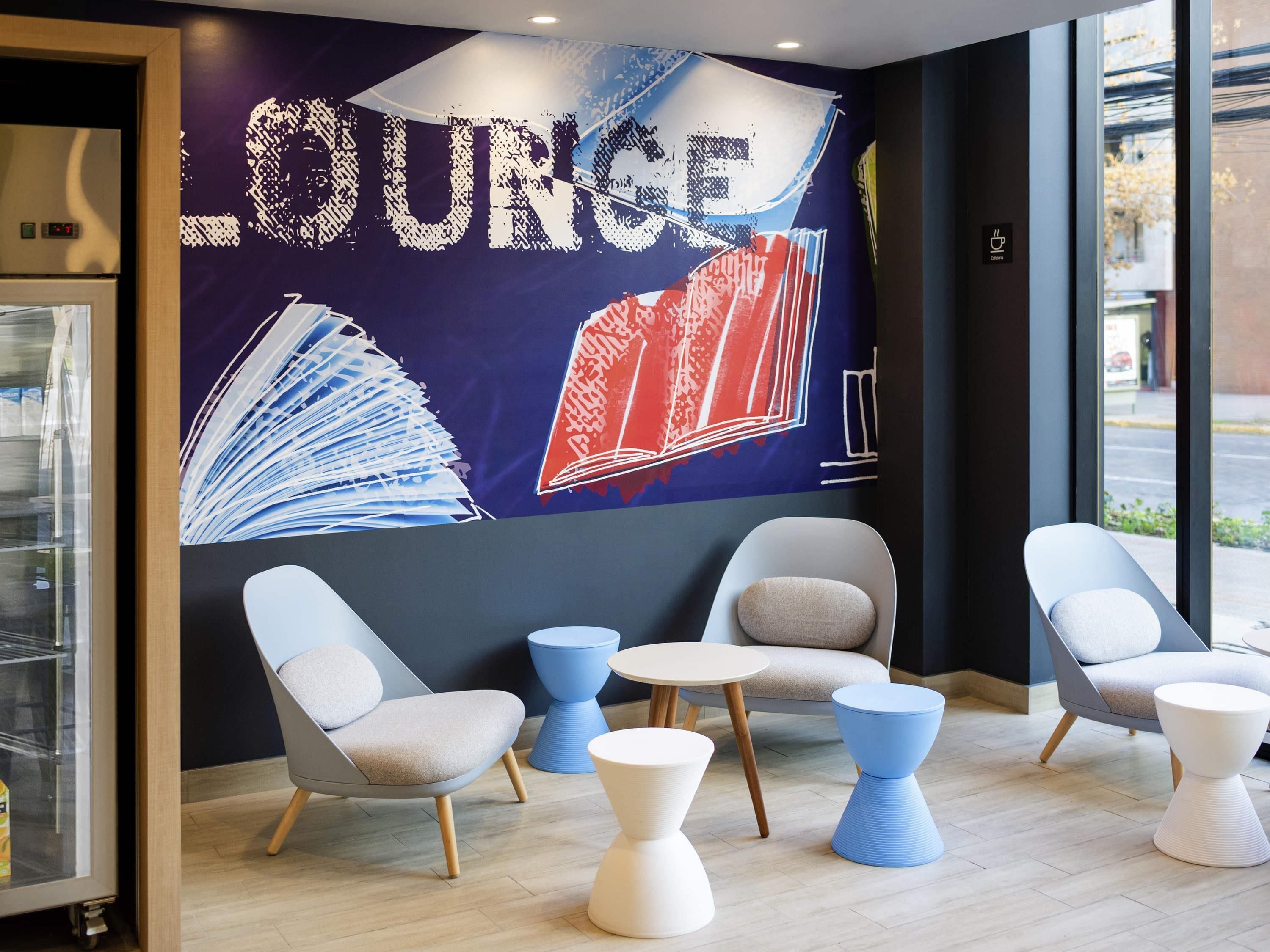 A lounge area with a large wall mural, seating arrangements, and a view through the window.