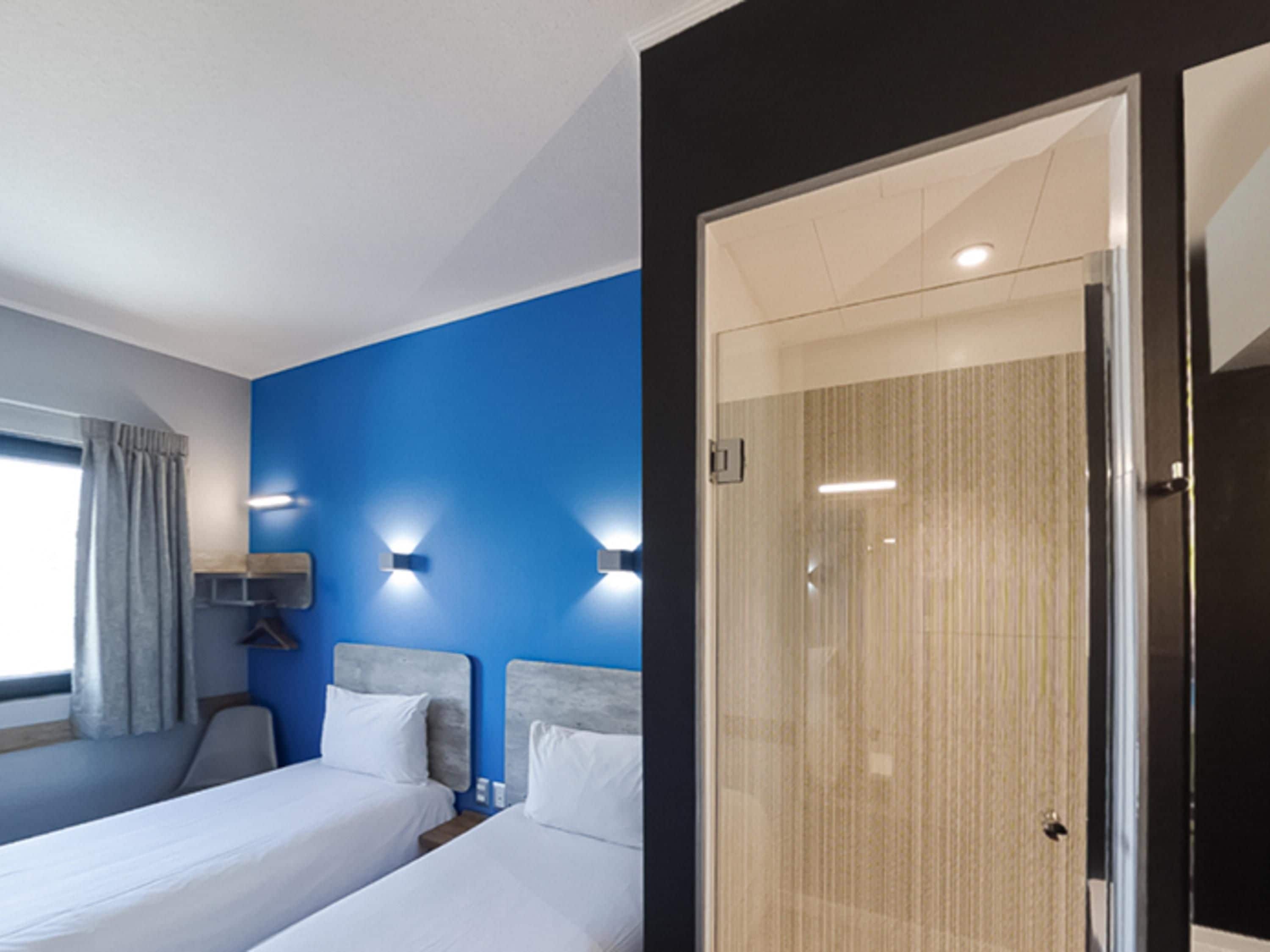A hotel room with two beds, a shower, and a window with curtains.