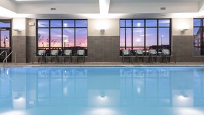A swimming pool with chairs and tables, large windows with a sunset view, and an exit sign. - Residence Inn by Marriott Minneapolis Maple Grove/Arbor Lakes (Maple Grove)