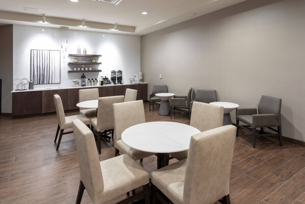 A modern dining area with round tables and chairs, a kitchen in the background, and a neutral color scheme.