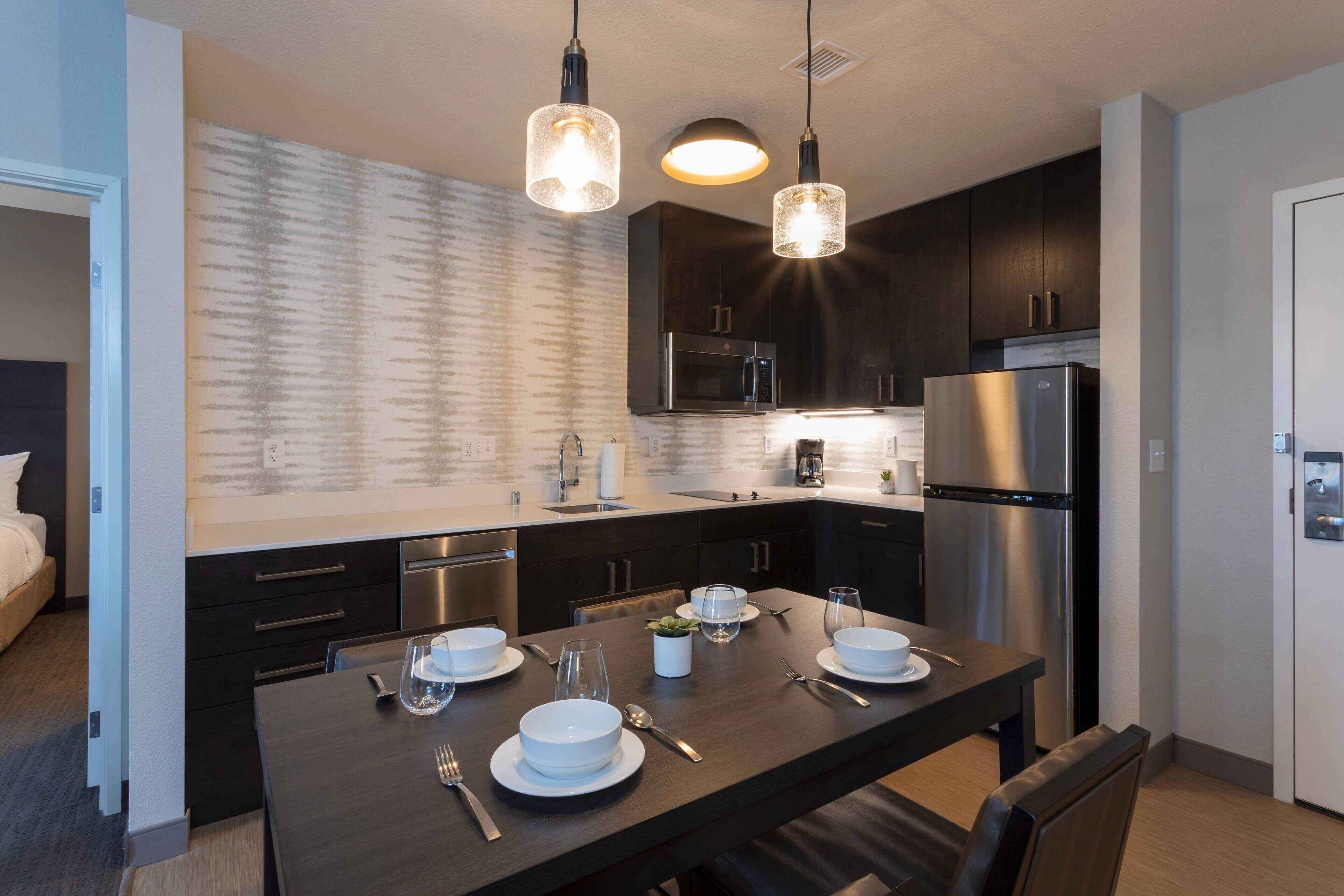 Une cuisine moderne avec des meubles de couleur sombre, des appareils en acier inoxydable et des luminaires suspendus.