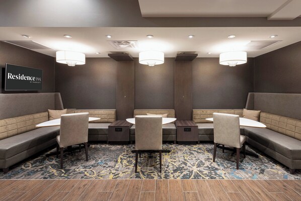 A conference room with a round table, four chairs, and a sofa. There are ceiling lights and a sign that reads "Residence Inn by Marriott".