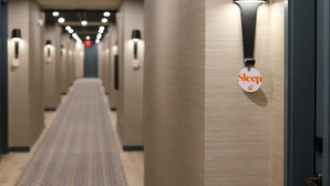 Een hotelgang met een geruit tapijt, wandlampen en een bordje dat een slaapgedeelte aangeeft.